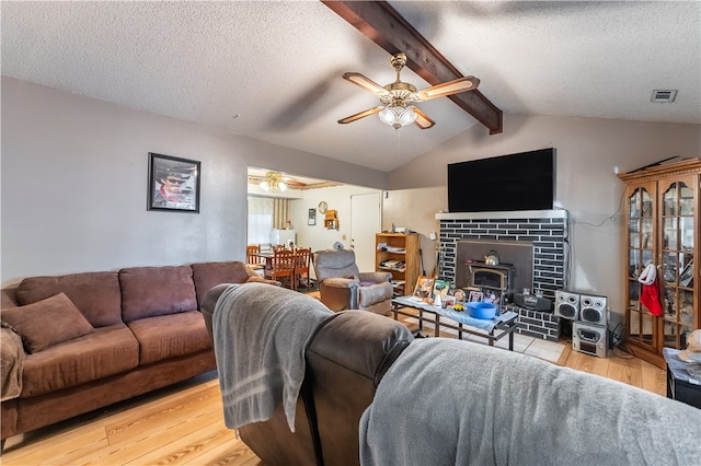 living room with ceiling fan, a textured ceiling, light hardwood / wood-style flooring, a wood stove, and lofted ceiling with beams