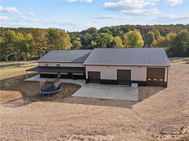 view of front facade featuring a trampoline, metal roof, a wooded view, a garage, and driveway