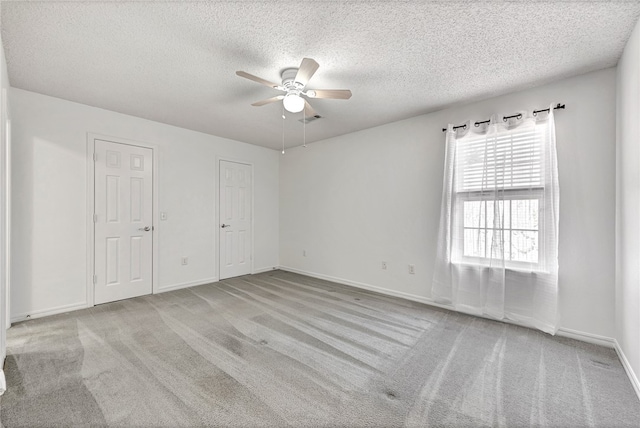 unfurnished bedroom with a textured ceiling, two closets, light colored carpet, and ceiling fan