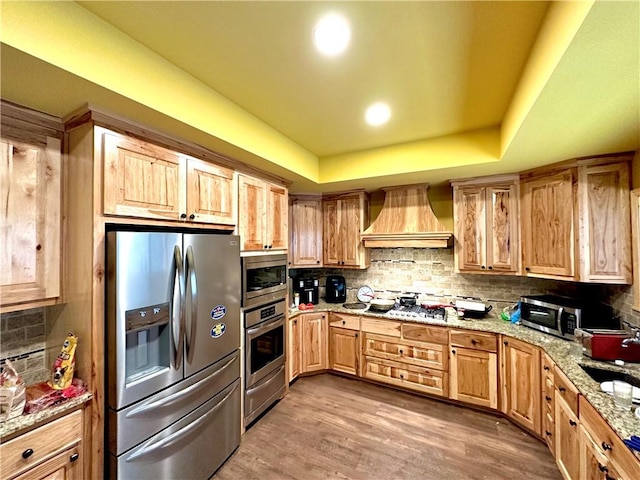 kitchen featuring stainless steel appliances, light brown cabinets, custom range hood, tasteful backsplash, and light stone counters