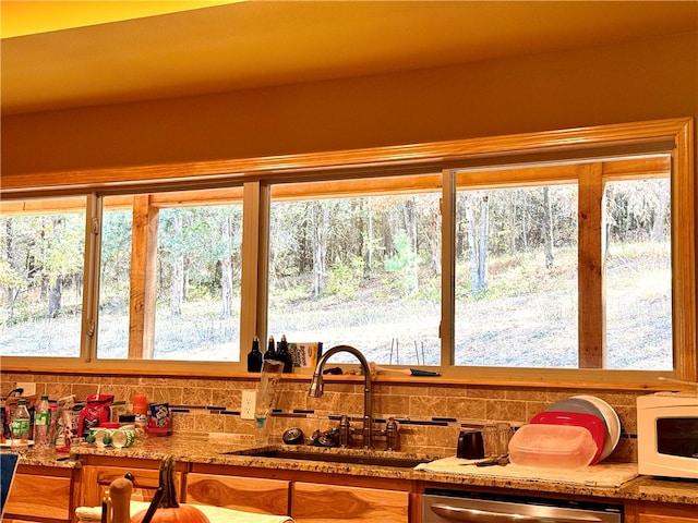 interior space featuring stainless steel dishwasher, sink, decorative backsplash, and light stone countertops