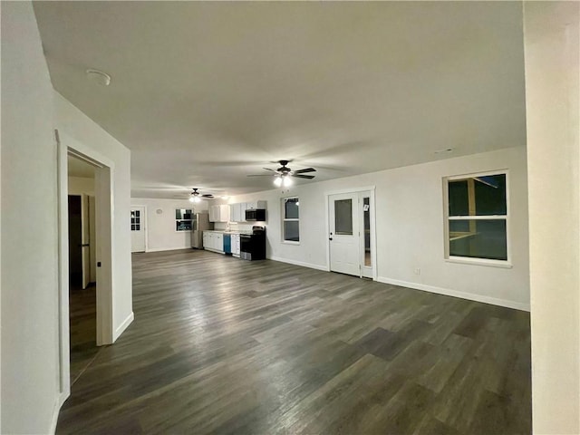 unfurnished living room with baseboards, ceiling fan, and dark wood-style flooring