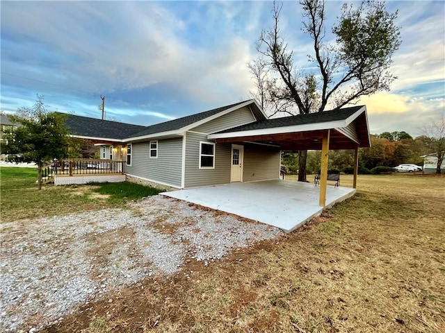 rear view of property featuring gravel driveway, an attached carport, and a lawn