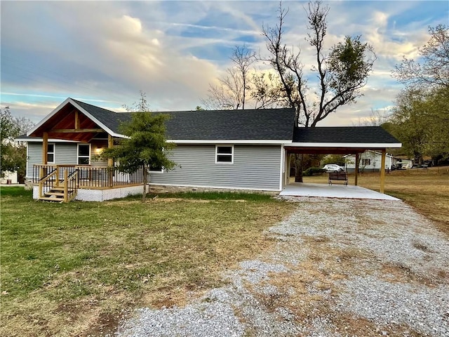 view of front facade with an attached carport, covered porch, a front yard, roof with shingles, and gravel driveway