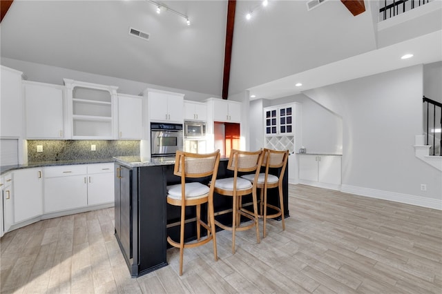 kitchen featuring beamed ceiling, a center island, light stone countertops, and white cabinetry