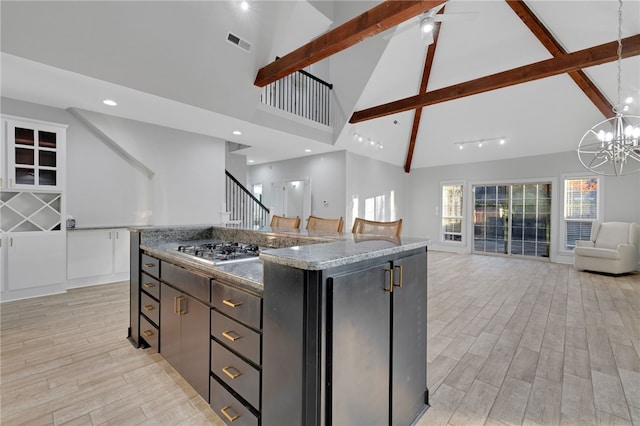 kitchen featuring stainless steel gas stovetop, high vaulted ceiling, dark stone countertops, light wood-type flooring, and a kitchen island