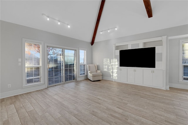 unfurnished living room featuring vaulted ceiling with beams, a wealth of natural light, and light hardwood / wood-style flooring