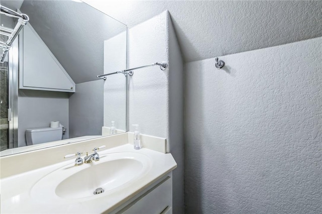 bathroom featuring a textured ceiling, vanity, toilet, and lofted ceiling