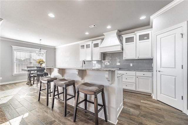 kitchen with a center island with sink, light stone countertops, custom exhaust hood, and white cabinets