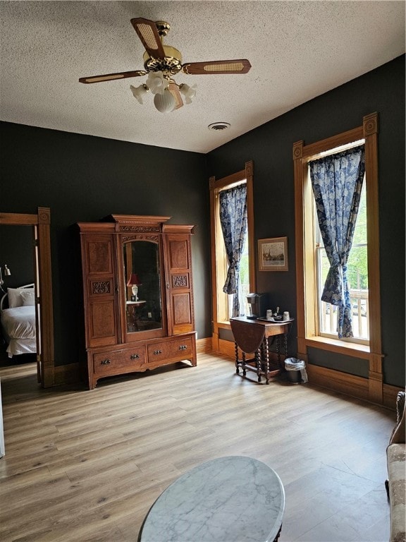 living area with light hardwood / wood-style floors, a textured ceiling, and ceiling fan