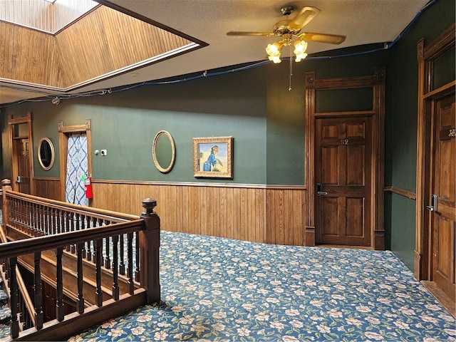 stairs with ceiling fan, a textured ceiling, and wooden walls