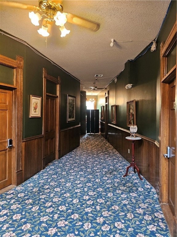 hallway featuring carpet, wood walls, and a textured ceiling