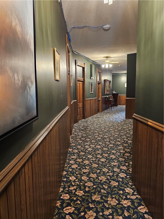 corridor with carpet flooring, a textured ceiling, and wooden walls