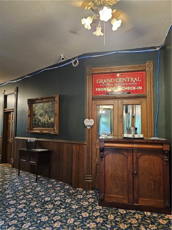 interior details featuring ceiling fan, wood walls, a textured ceiling, and carpet floors