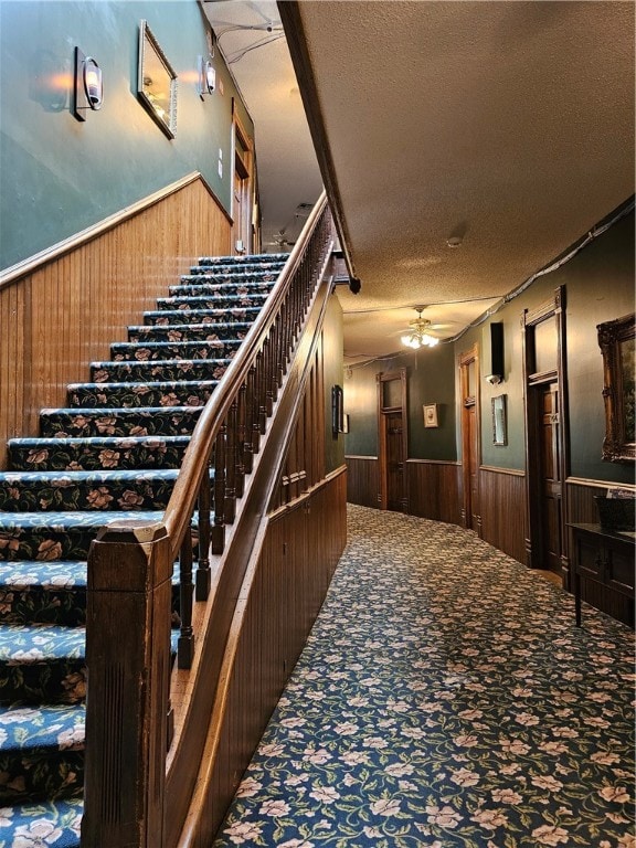 stairway featuring wooden walls, a textured ceiling, carpet floors, and ceiling fan