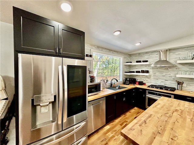 kitchen with wall chimney range hood, appliances with stainless steel finishes, sink, wood counters, and vaulted ceiling