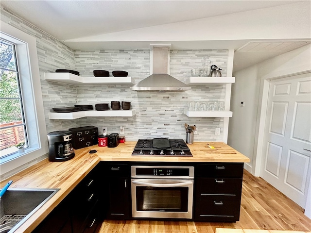 kitchen with oven, wood counters, wall chimney exhaust hood, decorative backsplash, and black gas stovetop