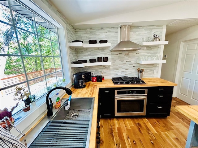 kitchen with backsplash, wood counters, stainless steel oven, wall chimney exhaust hood, and black gas cooktop