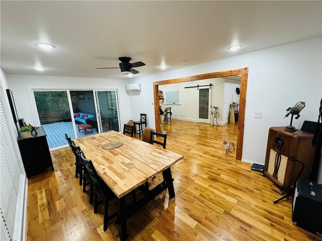 dining room featuring ceiling fan, wood-type flooring, a wall mounted air conditioner, and a barn door