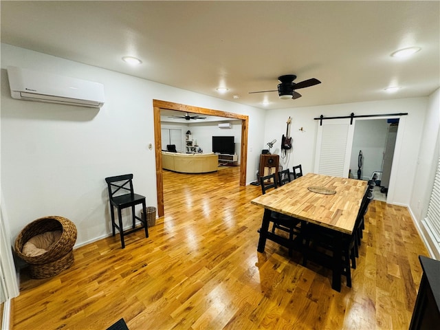 dining space with a wall mounted AC, a barn door, and light hardwood / wood-style flooring