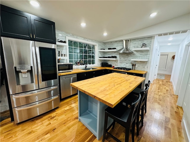 kitchen with a kitchen island, appliances with stainless steel finishes, a kitchen breakfast bar, wall chimney exhaust hood, and wooden counters