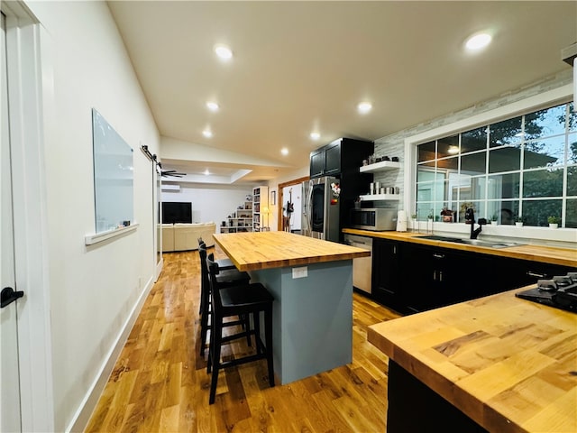 kitchen with a kitchen breakfast bar, wood counters, a center island, appliances with stainless steel finishes, and light hardwood / wood-style floors