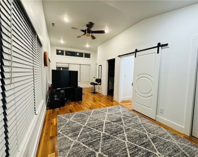 bedroom with ceiling fan, a barn door, wood-type flooring, vaulted ceiling, and a closet