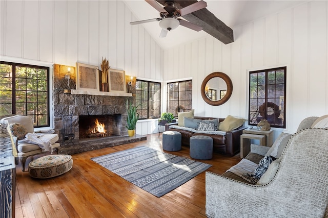 living room featuring ceiling fan, beam ceiling, high vaulted ceiling, hardwood / wood-style floors, and a stone fireplace