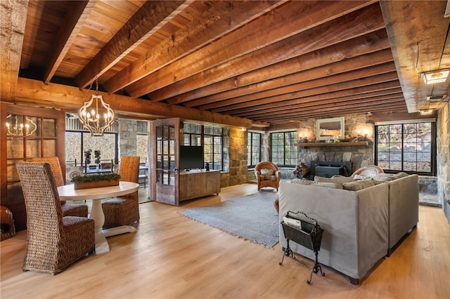 living room featuring wood ceiling, beam ceiling, an inviting chandelier, light hardwood / wood-style flooring, and a stone fireplace