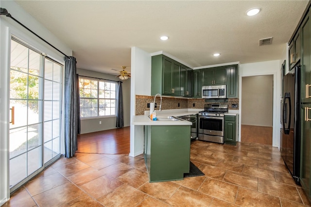 kitchen featuring kitchen peninsula, appliances with stainless steel finishes, tasteful backsplash, ceiling fan, and green cabinetry