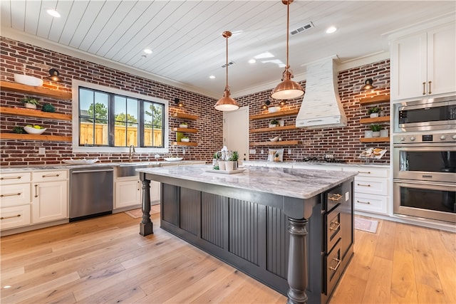 kitchen featuring hanging light fixtures, stainless steel appliances, white cabinets, and brick wall