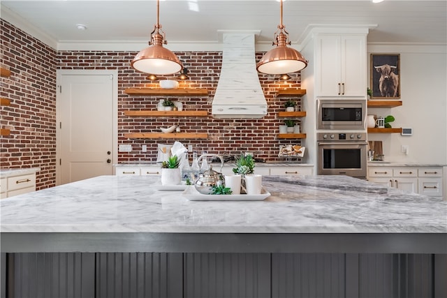 kitchen featuring pendant lighting, brick wall, appliances with stainless steel finishes, and white cabinetry