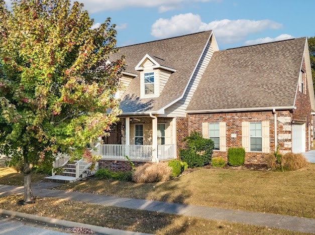 new england style home featuring covered porch, a front yard, and a garage