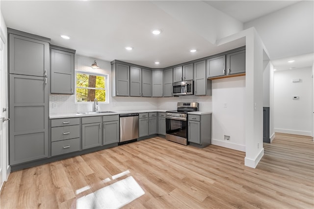 kitchen featuring light hardwood / wood-style floors, decorative backsplash, sink, gray cabinetry, and appliances with stainless steel finishes