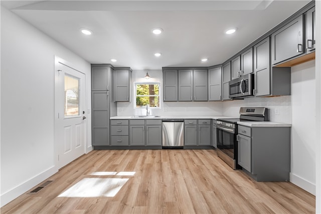 kitchen with light hardwood / wood-style floors, sink, appliances with stainless steel finishes, backsplash, and gray cabinetry