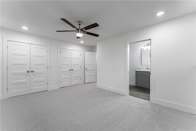 unfurnished bedroom featuring ensuite bath, light colored carpet, sink, ceiling fan, and multiple closets