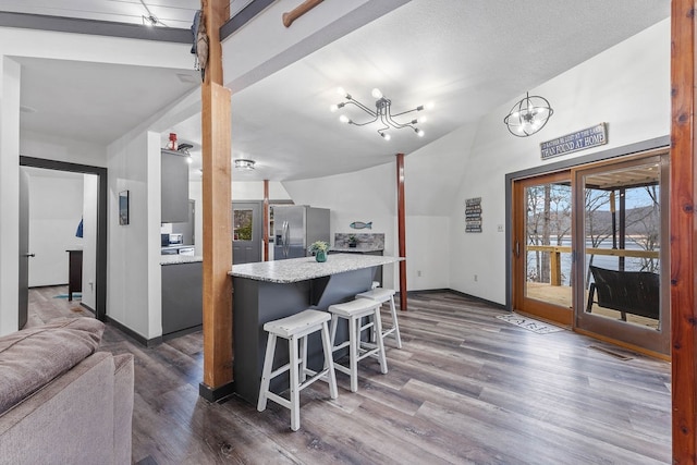 kitchen featuring a breakfast bar area, stainless steel refrigerator with ice dispenser, vaulted ceiling, an inviting chandelier, and dark hardwood / wood-style flooring