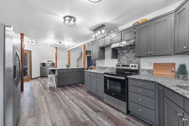 kitchen with gray cabinets, appliances with stainless steel finishes, light stone countertops, and dark hardwood / wood-style flooring