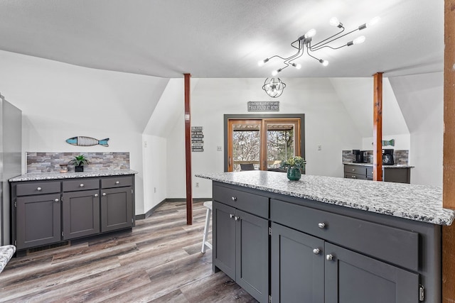 kitchen with lofted ceiling, tasteful backsplash, a chandelier, dark hardwood / wood-style floors, and gray cabinets