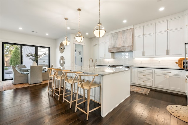 kitchen featuring white cabinets, a center island with sink, dark stone counters, dark wood-type flooring, and decorative light fixtures