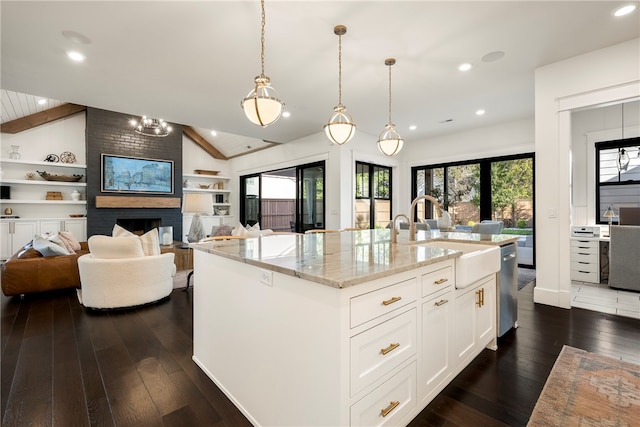 kitchen featuring light stone countertops, sink, lofted ceiling with beams, white cabinetry, and a kitchen island with sink