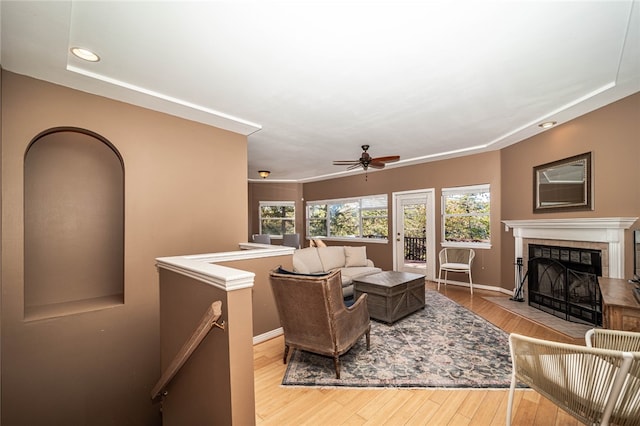 living room featuring a tiled fireplace, ceiling fan, and light hardwood / wood-style flooring