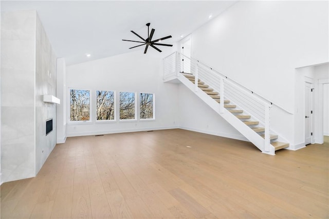 unfurnished living room featuring a fireplace, high vaulted ceiling, ceiling fan, and light hardwood / wood-style flooring