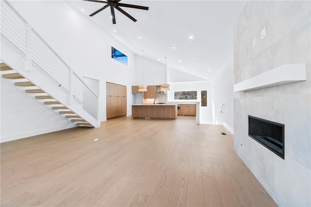 unfurnished living room featuring a tile fireplace, high vaulted ceiling, light hardwood / wood-style flooring, and ceiling fan