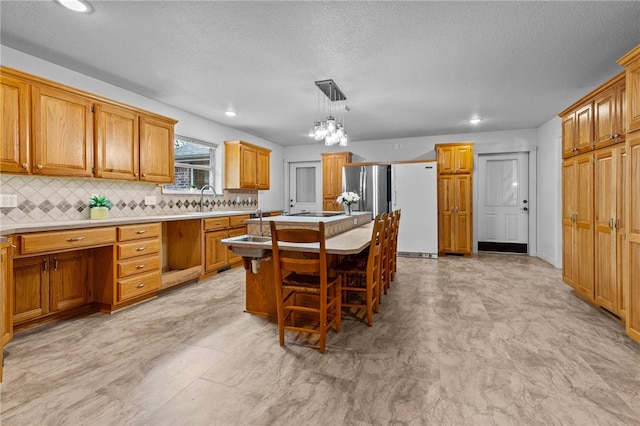 kitchen featuring tasteful backsplash, a kitchen island, fridge, hanging light fixtures, and a breakfast bar area