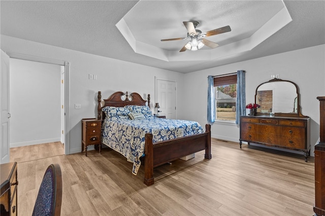 bedroom featuring ceiling fan, a textured ceiling, a tray ceiling, and light wood-type flooring