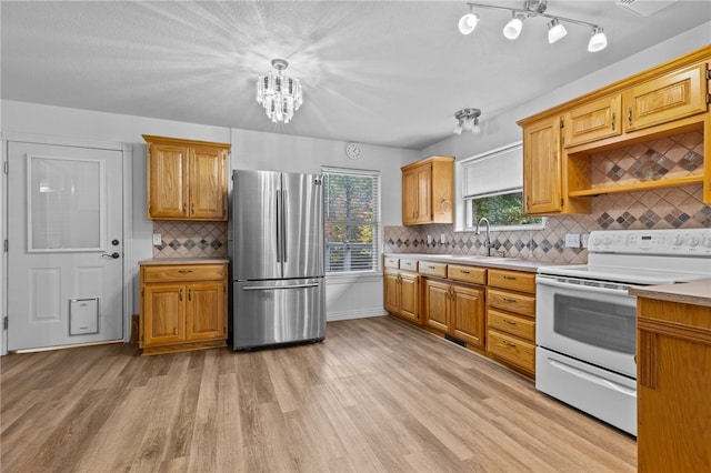 kitchen with electric range, decorative backsplash, hanging light fixtures, light hardwood / wood-style floors, and stainless steel refrigerator