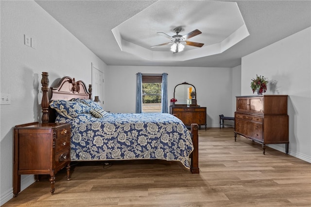 bedroom featuring ceiling fan, a textured ceiling, a tray ceiling, and light hardwood / wood-style floors