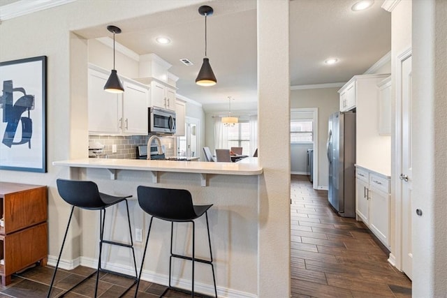 kitchen featuring white cabinetry, ornamental molding, stainless steel appliances, and a kitchen breakfast bar