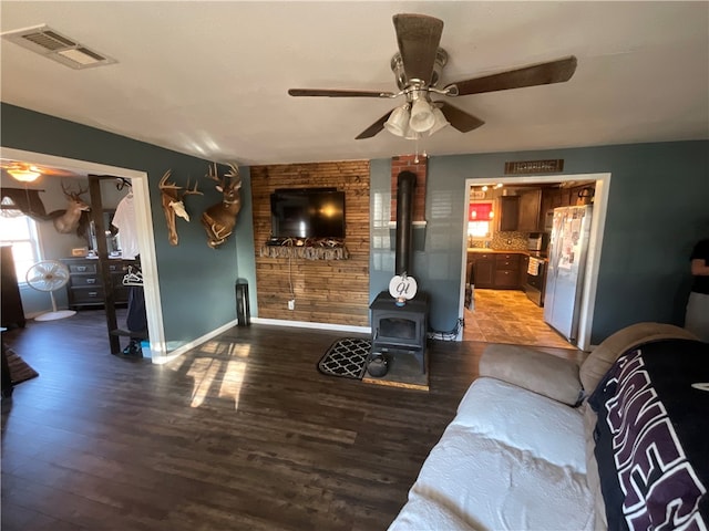 living room with dark hardwood / wood-style floors, a wood stove, and ceiling fan